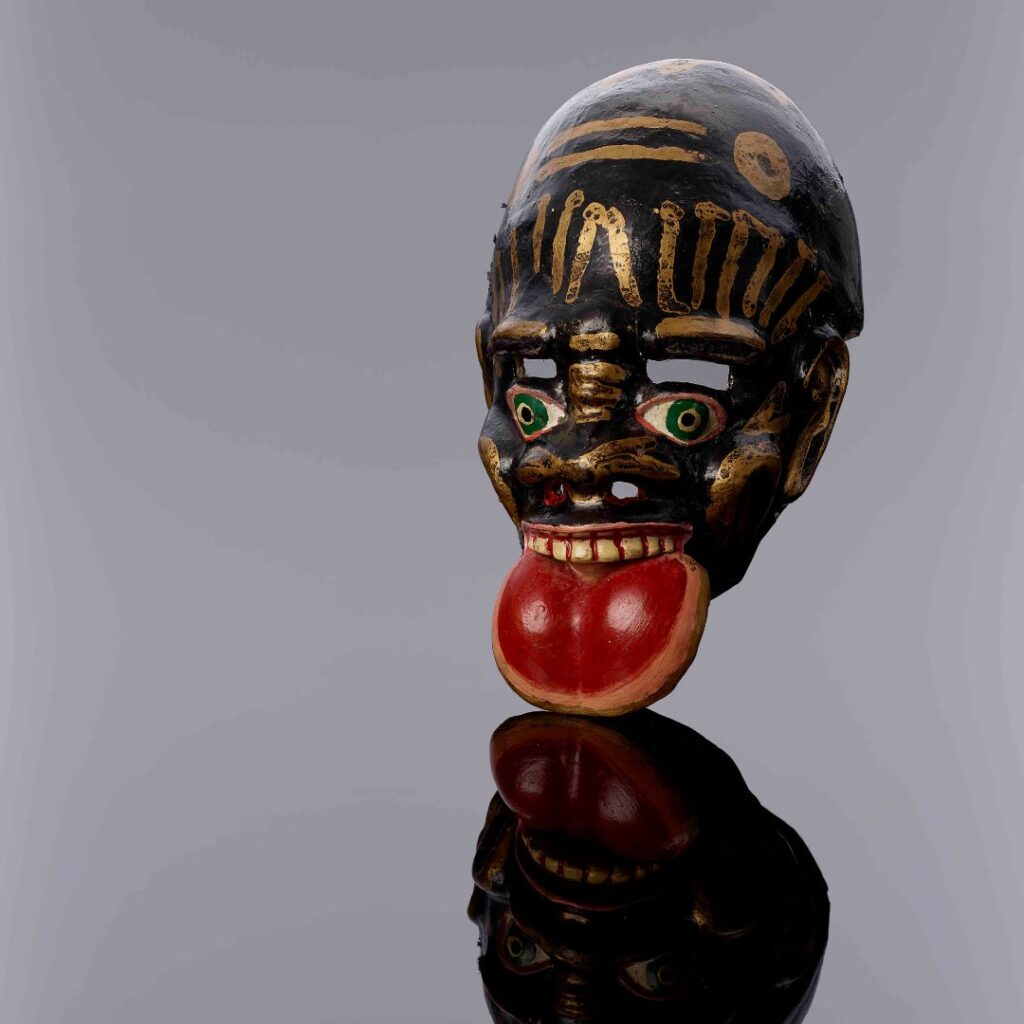 Human face mask with prominent mouth and tongue. Painted in black, gold and red colours, it is used to depict afrodescendants in Andean carnival dances