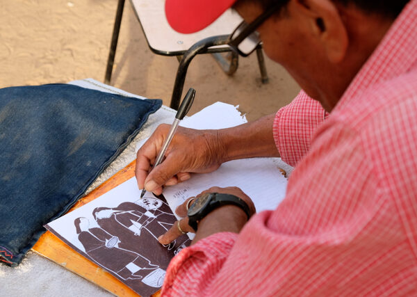 Image of a man drawing on a white paper with a black pen